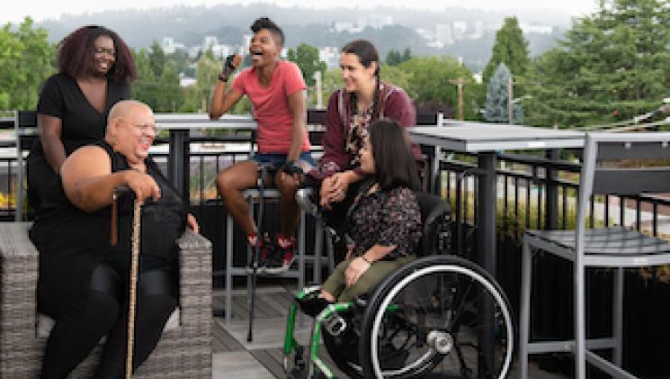Photo Credit: Disabled and Here https://affecttheverb.com/gallery/disabledandhere/deckcity/ BIPOC Disabled Friends Laughing Outdoors