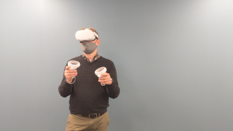 Dr. Mike Reid wearing white VR goggles, holding two controllers, and a face mask