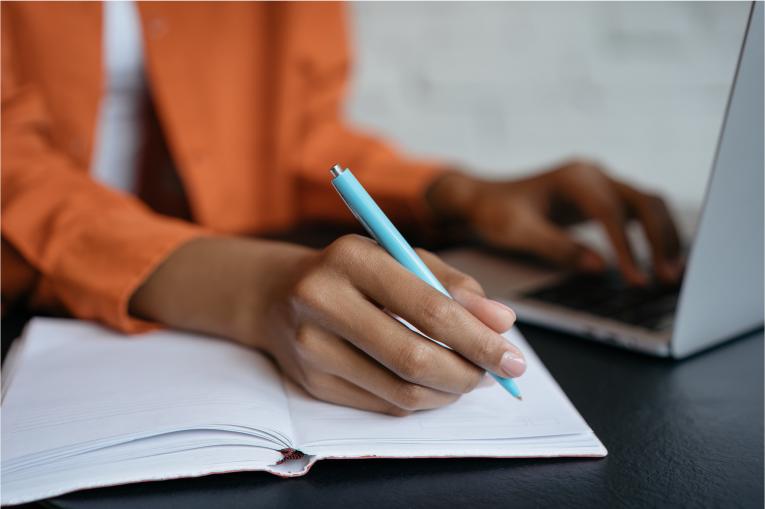 person taking notes in a notebook and using a computer