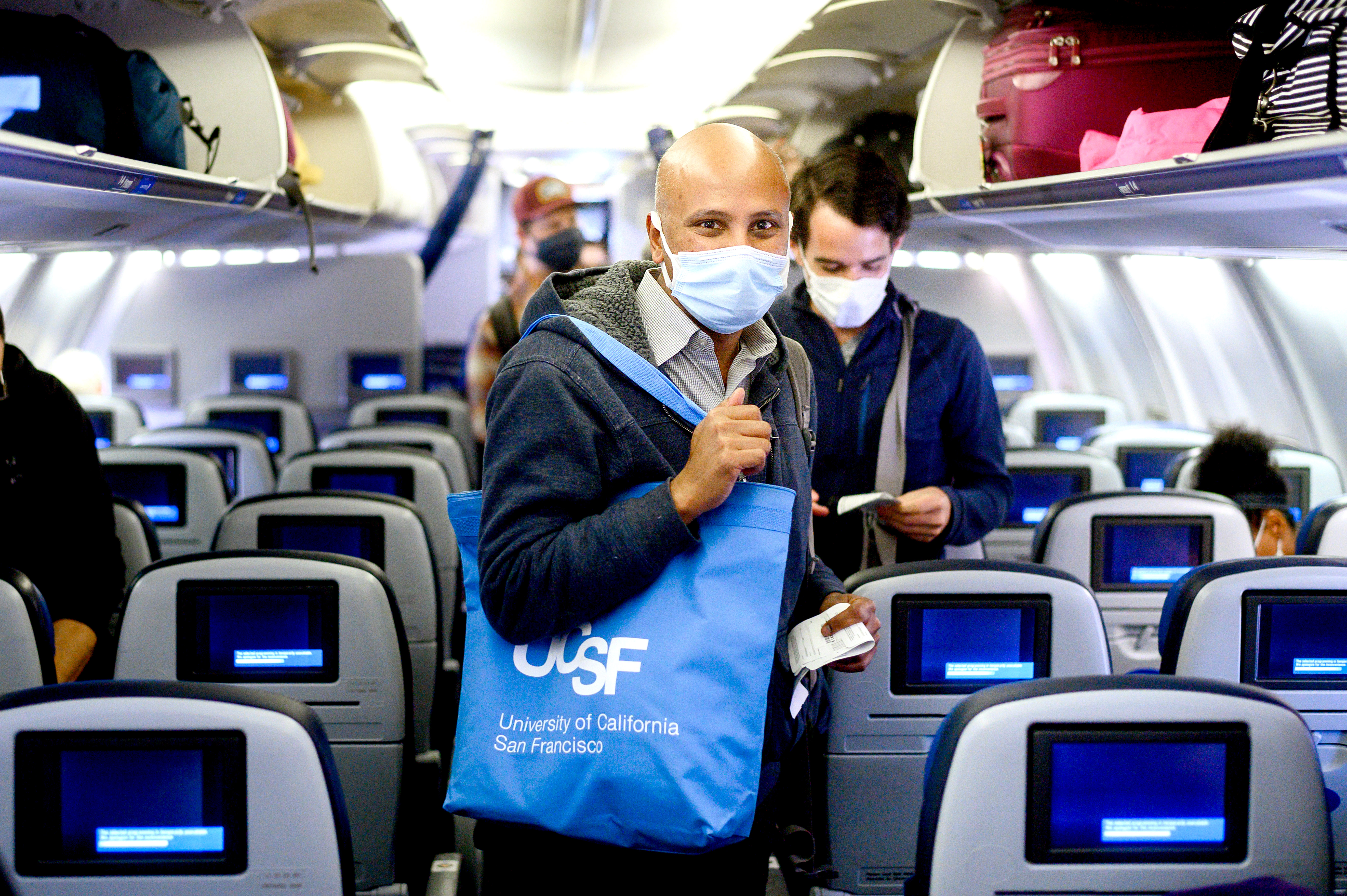 Man on a plane with a face mask and UCSF tote bag