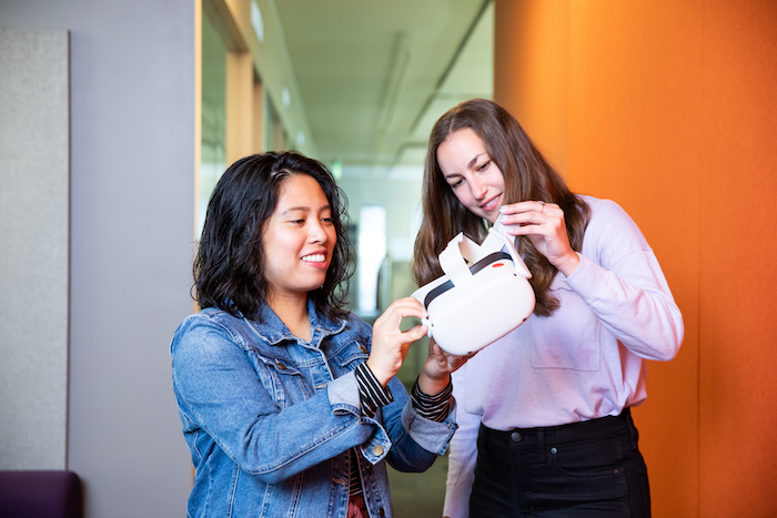 Lynhea Anicete of CULTIVATE shows Taytum Sanderbeck how to use the white VR goggles.