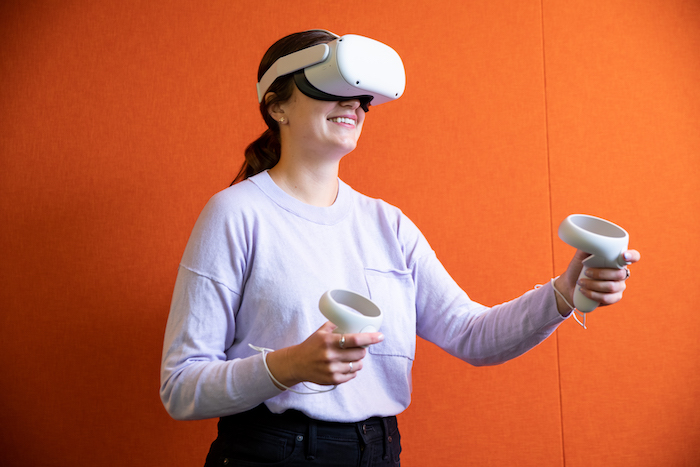 Taytum Sanderbeck wearing white VR goggles and holding a round, white controller in each hand